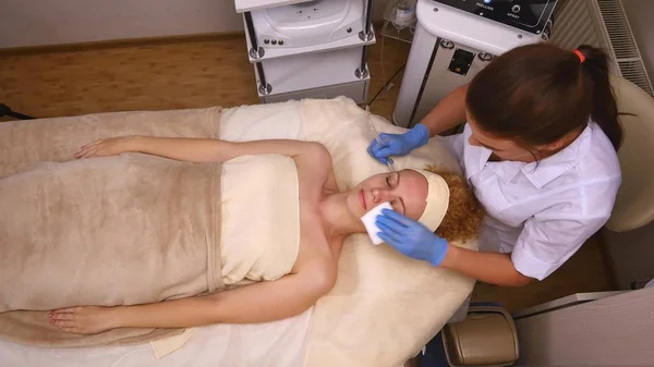 Joven hermosa mujer acostada en la mesa clínica, el cosmetólogo le hace un masaje de electro-estimulación facial. Procedimiento de elevación, cosmetología de hardware. Estilo de vida de lujo, actividades modelo. Parte superior — Foto de Stock