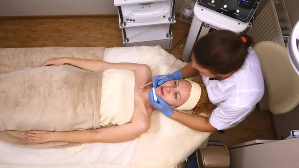 Junge schöne Frau auf dem klinischen Tisch liegend, macht ihr der Kosmetologe eine Gesichtsmassage mit Elektrostimulation. Hebeverfahren, Hardware-Kosmetologie. Luxus-Lifestyle, Modelaktivitäten. oben — Stockfoto