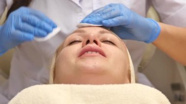 Güzel bir kadın kozmetik masanın üzerinde profesyonel olarak hastanın yüz temizlemek için pamuk sünger kullanarak dermatolog yatan Kapalı gözlerle. Yüz bakımı, sağlıklı olmak mutlu olmak,