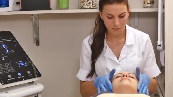 Kosmetikerin Creme auf das Gesicht und massiert Frau, die kosmetische Behandlung im Spa. professionelle Kosmetikerin Anwendung Maske auf weibliche im Schönheitssalon. Gesichtsbehandlung Reinigung Kosmetologie der Haut — Stockvideo