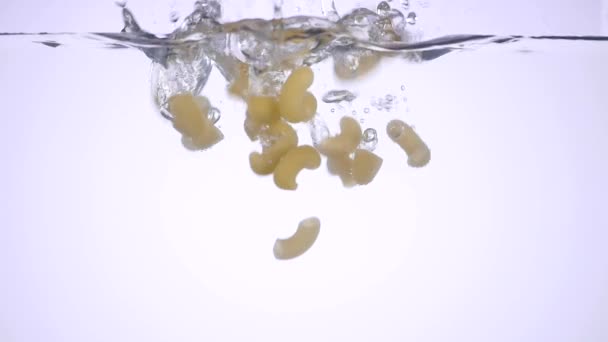 Salpicadura de pasta de macarrones cayendo en agua hervida sobre fondo blanco, la nutrición italiana y el concepto de cuidado de la salud. vista inferior — Vídeos de Stock