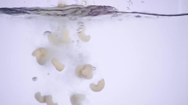 Salpicadura de pasta de macarrones cayendo en agua hervida sobre fondo blanco, nutrición italiana y concepto de cuidado de la salud — Vídeo de stock