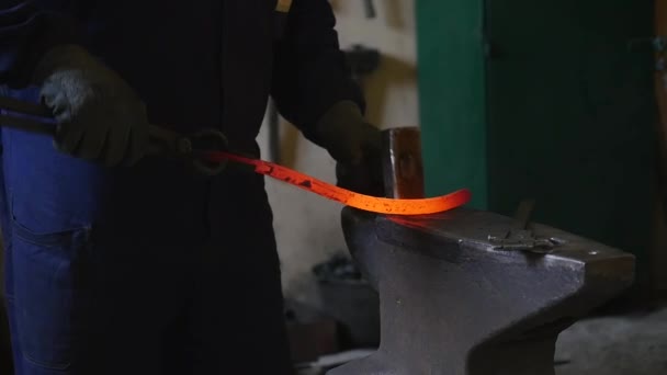 Blacksmith bends an iron hot stick with a hammer — Stock Video