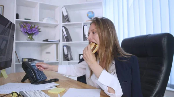 Mujer ocupada hablando por teléfono mientras toma una hamburguesa — Foto de Stock