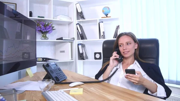 Young attractive businesswoman talking on telephone and using smartphone in the office and smiling — Stock Photo, Image