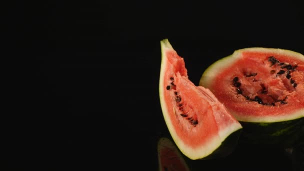 På en halv en vattenmelon ligger en triangulär bit vattenmelon, Närbild svart bakgrund — Stockvideo