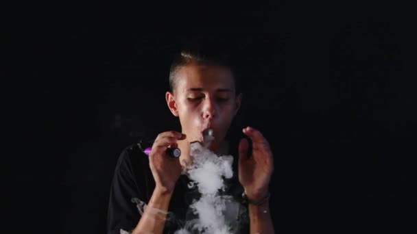 De man rook elektrische sigaret tegen de donkere achtergrond — Stockvideo