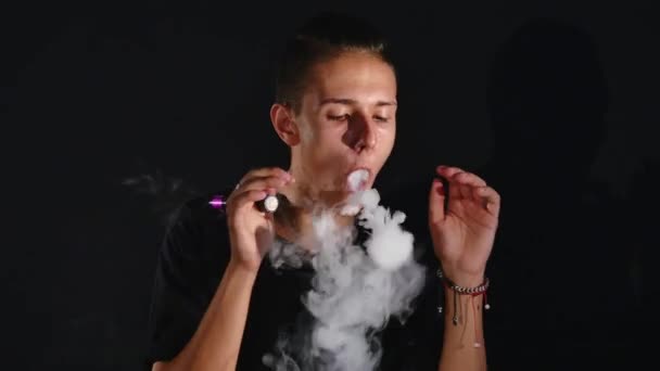 Человек курит электрическую сигарету на темном фоне — стоковое видео