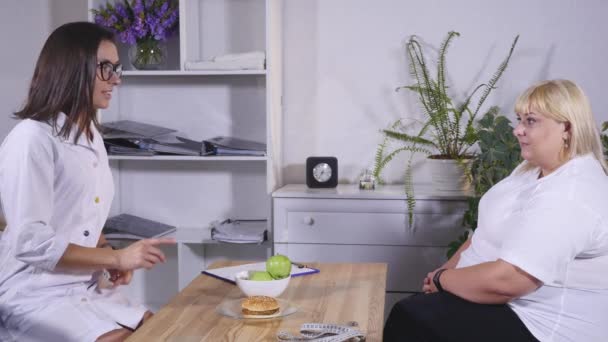 En nutritionist förklarar klienten om hamburgare och äpplen — Stockvideo