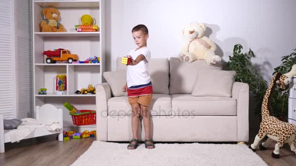 Мальчик собирает кубик рубика и указывает на камеру — стоковое видео