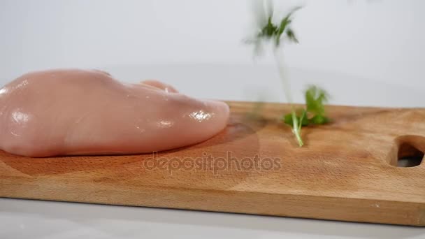Filete de pollo crudo y perejil cae sobre una tabla de madera — Vídeos de Stock