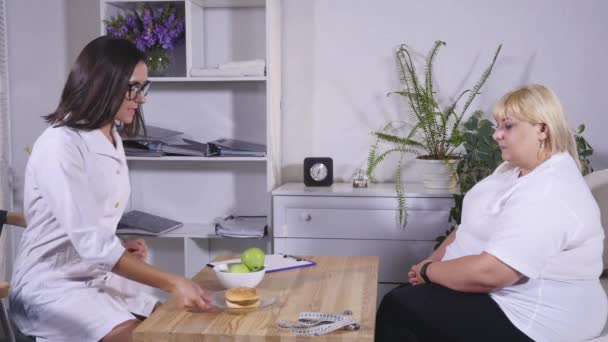 En nutritionist förklarar klienten om hamburgare och äpplen — Stockvideo