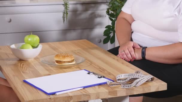 Un nutricionista le da manzanas y una hamburguesa a un cliente — Vídeo de stock