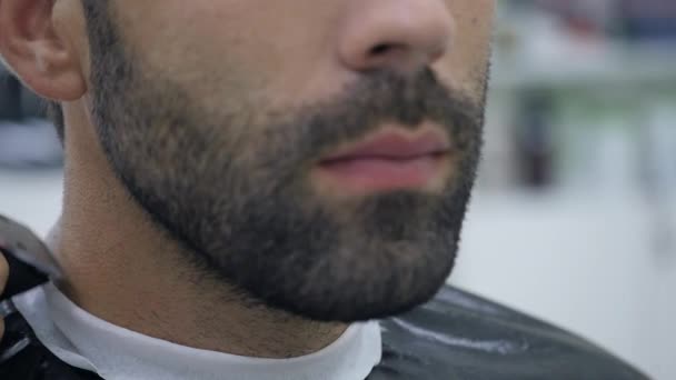 Hairstyling process. Close-up of a barber drying hair of a young bearded man — Stock Video