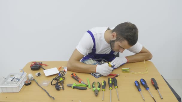 I workshopen elektrikern använder avbitare för att skära en bit tråd. Två män rymliga och ljusa studio arbetet bakom skrivbord av trä. I mitten av befälhavaren förkortar den vita kabeln — Stockvideo