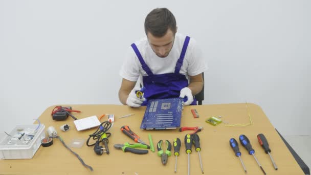 En el taller electricista utilizando cortadores de alambre para cortar un trozo de alambre. Los dos hombres estudio amplio y luminoso trabajo detrás de un escritorio de madera. En el centro del maestro acorta el cable blanco — Vídeos de Stock