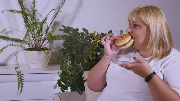 Donna grassa mangiare un hamburger, guardare la TV e ride — Foto Stock