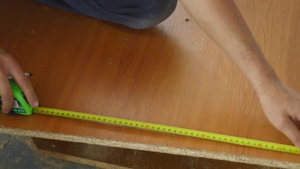 El hombre mide la longitud del tablero con una cinta métrica y hace una marca de lápiz — Vídeos de Stock