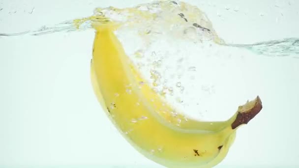 Plátanos sumergiéndose en el agua sobre fondo blanco en cámara lenta — Vídeo de stock