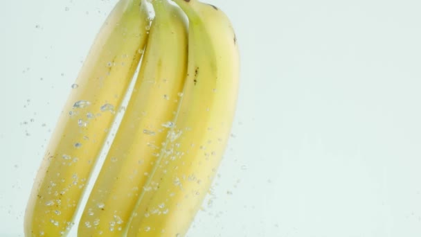 Μπανάνες που βυθίζονται στο νερό σε άσπρο φόντο σε αργή κίνηση — Αρχείο Βίντεο