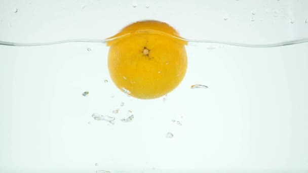 Целый апельсин медленно падает в воду — стоковое видео