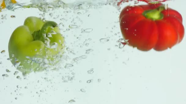 Red, green, yellow bell pepper falls to the water, causing bubbles and scattered water — Stock Video