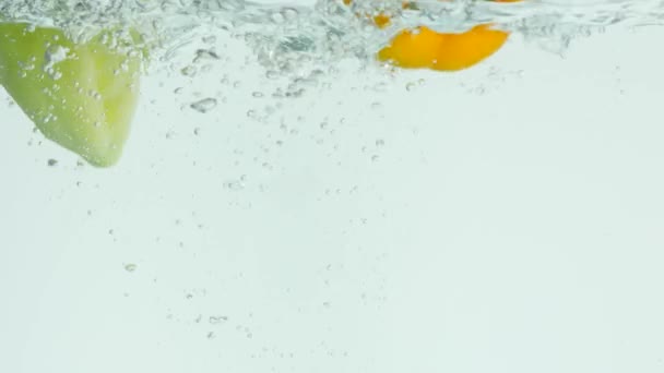 Vermelho, verde, pimentão amarelo cai para a água, causando bolhas e água dispersa — Vídeo de Stock
