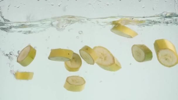 Banane fällt ins Wasser. Bananenstücke fallen unter Wasser auf weißem Hintergrund. frische gelbe Bananenfrucht stürzt und spritzt Wasser — Stockvideo