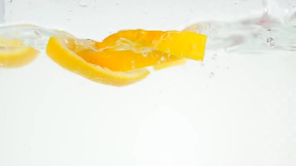 Cayendo en el agua y cayendo rodajas de naranja sobre un fondo blanco cámara lenta — Vídeos de Stock