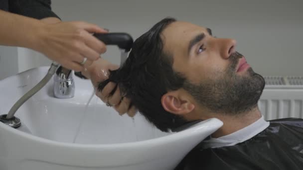 Las manos del peluquero vierten el agua a los clientes por el cabello. El cliente lava el cabello después de cortar en la peluquería. De cerca. 4K — Vídeos de Stock