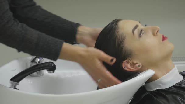 Peluquería lavar un cabello clientes en un lavabo moderno en su salón de peluquería mientras se prepara para peinar y cortar su cabello. de cerca — Vídeo de stock