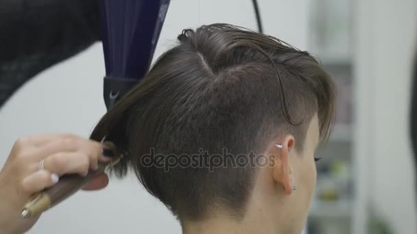 Uma jovem se senta em uma poltrona de cabeleireiro: um cabeleireiro faz um estilo de cabelo. Uma jovem mulher de cabelos justos veio ao salão de beleza para fazer um penteado elegante — Vídeo de Stock