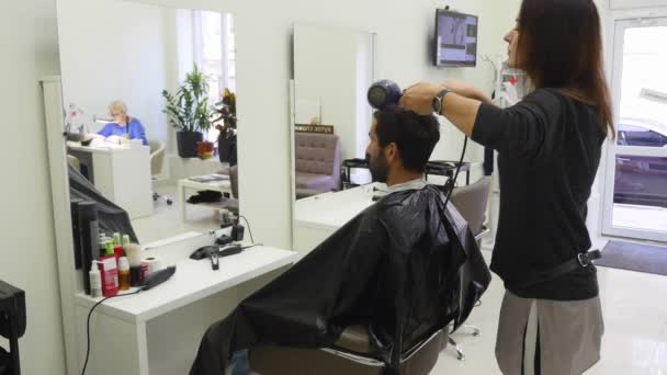 Peluquería profesional secando el cabello en el salón de belleza. Hombre joven cliente y hembra peluquero — Vídeo de stock
