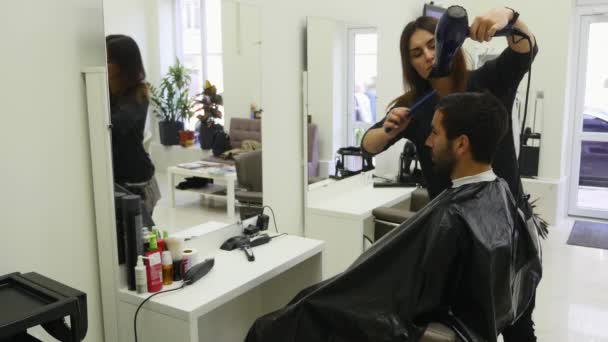 Професійний перукар сушить волосся в салоні краси. Чоловічий молодий клієнт і жіночий перукар — стокове відео