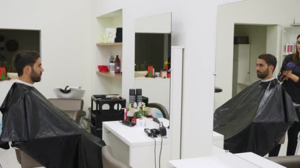 Professioneller Friseur trocknet die Haare im Schönheitssalon. männlicher junger Kunde und weibliche Friseurin — Stockvideo