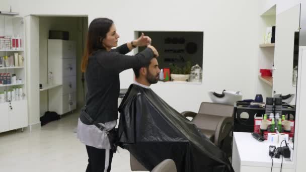Fryzjerzy kobieta i mężczyzna pracują z klientami z peleryny cięcia w salonie fryzjerskim — Wideo stockowe