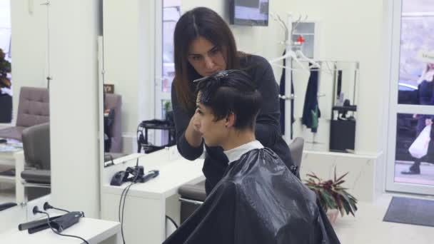 Una joven cortándose el pelo en la peluquería. Peluquero corta el pelo a una joven con una tijera profesional — Vídeo de stock