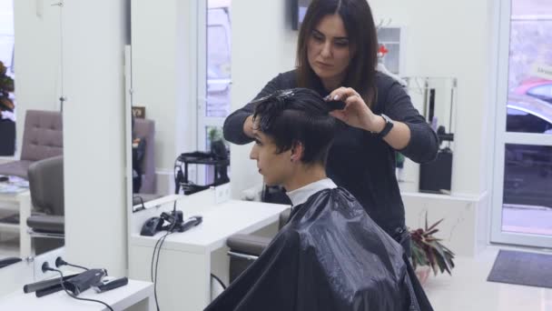 Jeune femme coupant les cheveux chez le coiffeur. Coiffeur coupe les cheveux à une jeune fille avec un ciseaux professionnels — Video