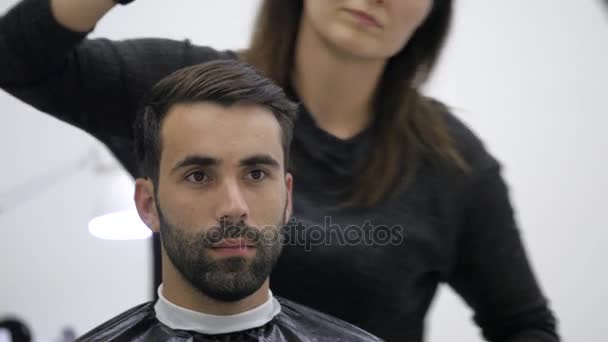 Alegre barbero hábil haciendo un corte de pelo con tijeras a un joven barbudo — Vídeo de stock