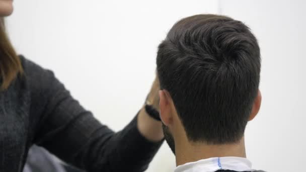 Alegre barbero hábil haciendo un corte de pelo con tijeras a un joven barbudo — Vídeos de Stock
