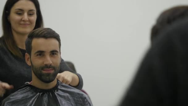 Профессиональный парикмахер показывает задний вид стрижки с помощью зеркала симпатичному довольному клиенту в профессиональной парикмахерской — стоковое видео