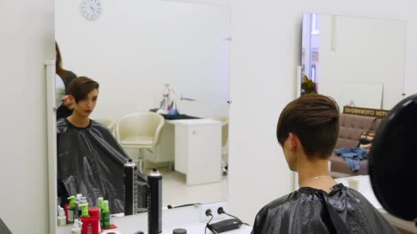 Cabeleireiro profissional mostra a visão traseira do corte de cabelo usando espelho para cliente feminino satisfeito bonito em uma barbearia de cabeleireiro profissional — Vídeo de Stock