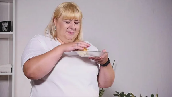 Dikke vrouw eten van een hamburger, kijkend naar de weegschaal en huilen, slow-motion — Stockfoto