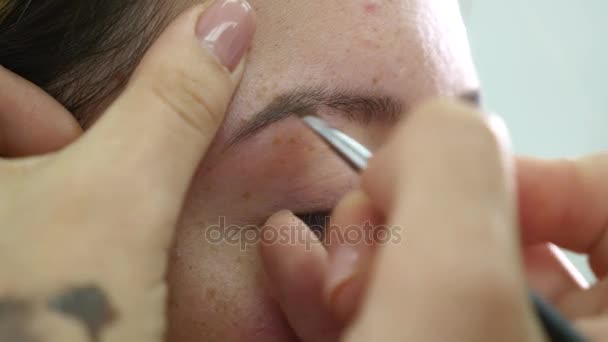 Vista de cerca de las manos de los maquilladores usando pincel para pintar cejas para un modelo con pestañas falsas — Vídeos de Stock