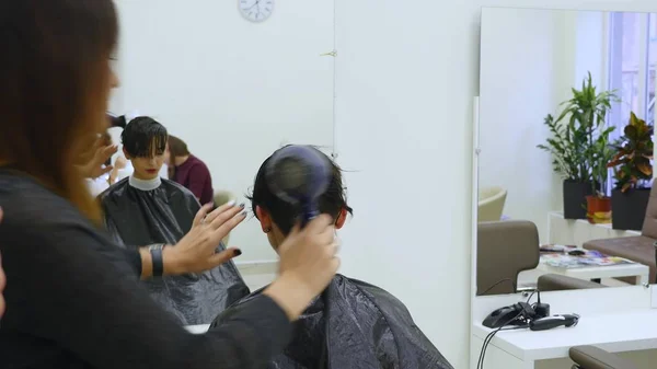 Penata rambut mengeringkan dan menyikat rambut wanita di salon rambut — Stok Foto