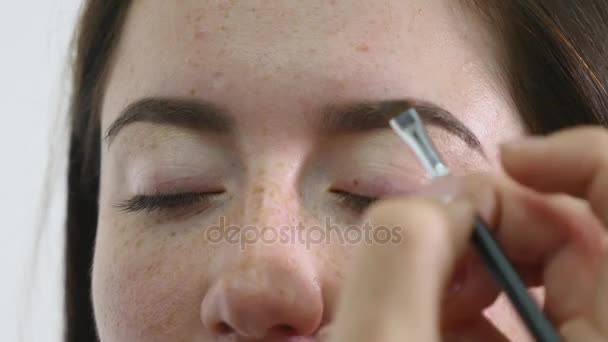 Artista de maquiagem pinta uma jovem menina sobrancelhas escuro pintura profissional — Vídeo de Stock