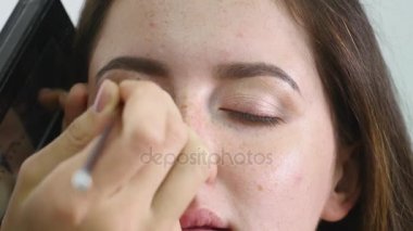 Genç profesyonel kadın photomodel çehresini Güzellik Salonu Makyaj süreci sırasında kapatın. Genç visagiste özel fırça kullanarak göz kapağı üzerinde göz farı uyguluyor