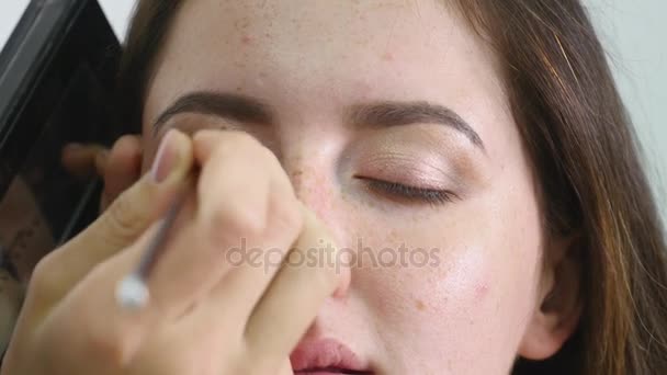 关闭一脸的年轻职业女性 photomodel 在美容店化妆过程。年轻的 visagiste 使用特殊的画笔的眼睑上涂了眼影突出 — 图库视频影像