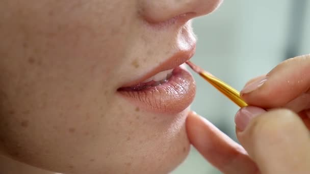 Closeup άποψη του ένας επαγγελματίας καλλιτέχνης μακιγιάζ εφαρμογή κραγιόν στα χείλη μοντέλα που εργάζονται στη βιομηχανία ομορφιά μόδα. Προβολή closeup ενός χεριού καλλιτέχνες χρησιμοποιώντας το ειδικό πινέλο. αργή κίνηση — Αρχείο Βίντεο