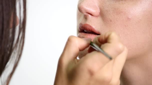 Closeup άποψη του ένας επαγγελματίας καλλιτέχνης μακιγιάζ εφαρμογή κραγιόν στα χείλη μοντέλα που εργάζονται στη βιομηχανία ομορφιά μόδα. Προβολή closeup ενός χεριού καλλιτέχνες χρησιμοποιώντας την ειδική βούρτσα — Αρχείο Βίντεο